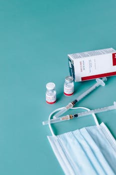 Close-up of COVID-19 vaccine vials, syringes, and a face mask against a blue background.