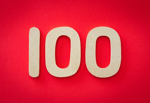 Close-up of numeral 100 in beige on a bright red background, emphasizing celebration.